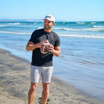 Man holding american football at the beach wearing CLVR Black Clover Live Lucky hat.