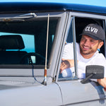 Man leaning out the window of his car wearing a Black Clover Live Lucky CLVR hat in white.