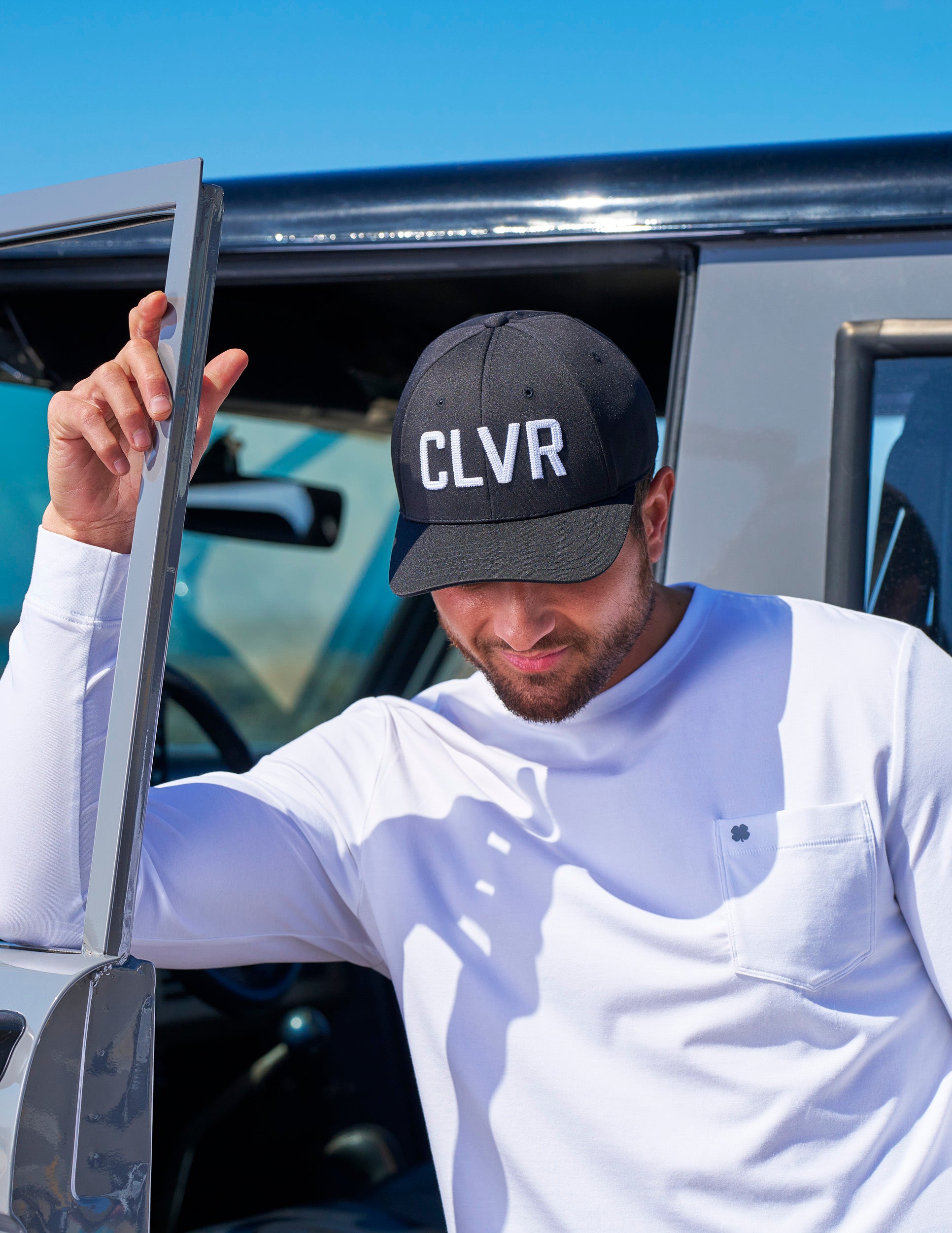 Man standing next to his car wearing a CLVR Black Clover Live Lucky hat in black.
