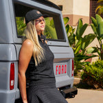Woman leaning against vintage truck wearing Black Clover Live Lucky Hollywood hat in black.